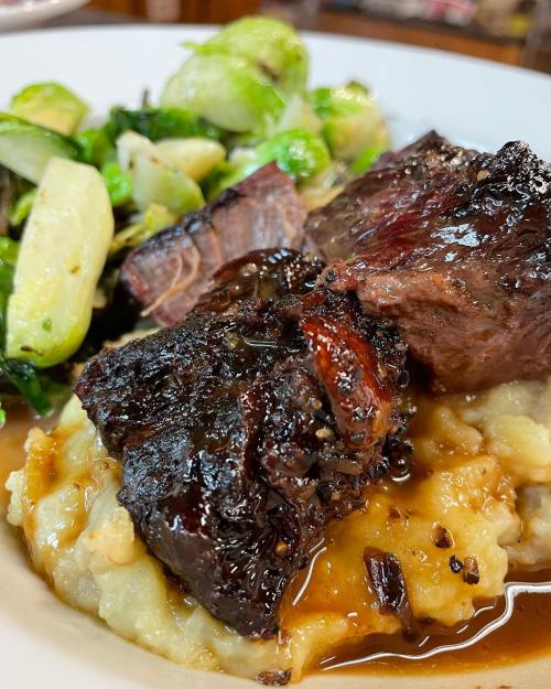 A plate featuring tender beef, creamy mashed potatoes, and sautéed vegetables, garnished with a rich sauce.