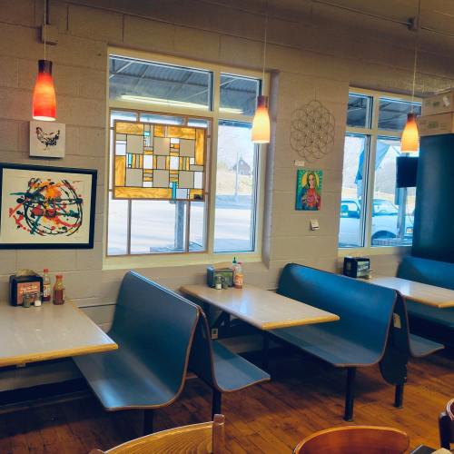 Cozy restaurant interior with blue booths, colorful artwork, and large windows letting in natural light.