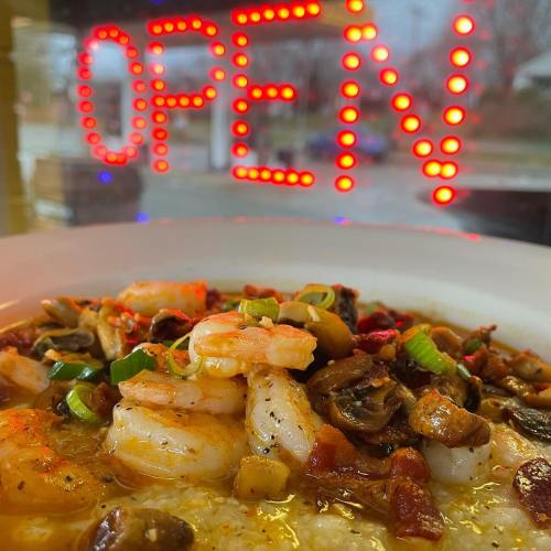A close-up of a shrimp dish with vegetables, in front of a bright "OPEN" sign.