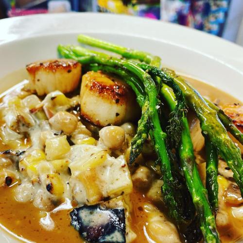 A creamy dish featuring seared scallops, asparagus, and a mix of vegetables in a rich sauce.