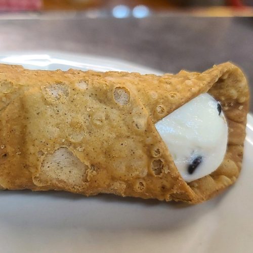 A close-up of a cannoli filled with creamy white filling and chocolate chips, resting on a white plate.