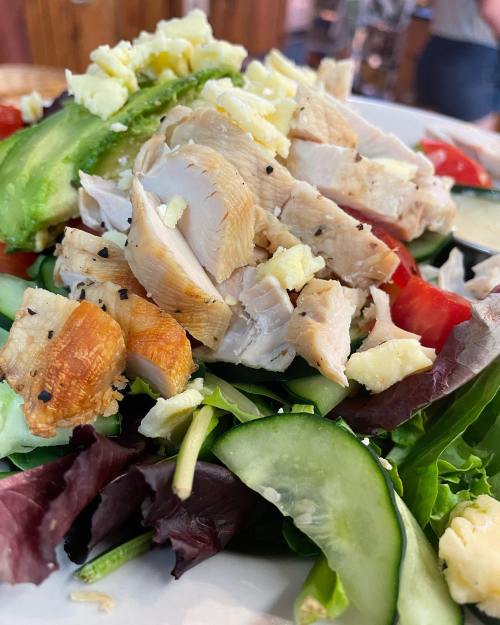 A fresh salad topped with sliced chicken, cucumbers, tomatoes, green peppers, and crumbled cheese on a bed of mixed greens.
