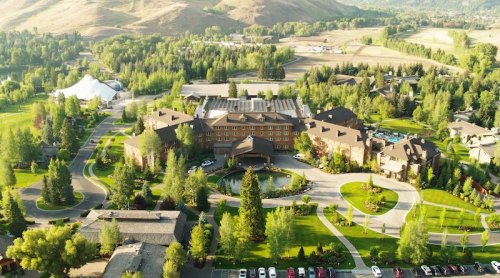 Aerial view of a large hotel surrounded by lush greenery and winding pathways, set against a mountainous backdrop.