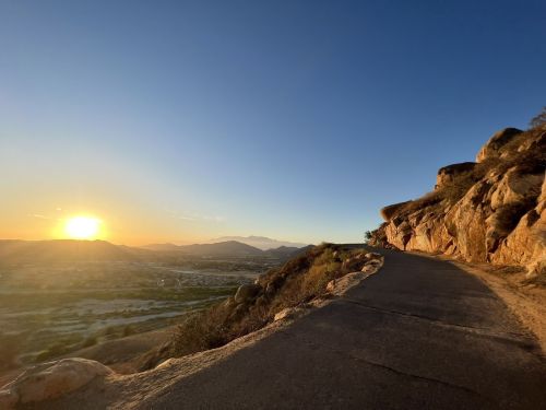 A winding road along rocky terrain with a sunset illuminating the landscape and mountains in the distance.