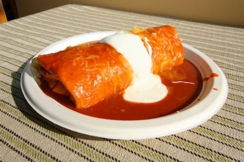 A plate of enchiladas topped with cheese and sour cream, served in a red sauce.