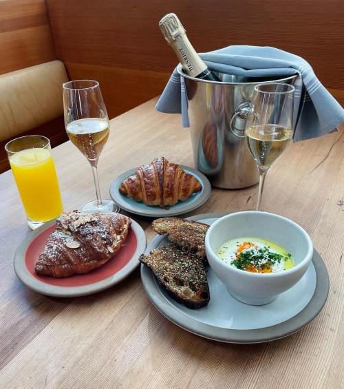 A table setting with two glasses of champagne, a bottle in an ice bucket, croissants, and a bowl of creamy dip with toast.