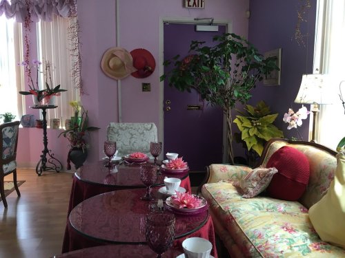 A cozy room with pink and purple walls, floral furniture, a sofa, and tables set with decorative dishes and plants.
