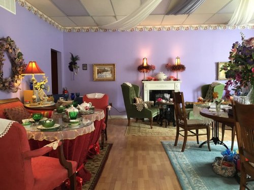 A cozy, pastel-colored tea room with elegant seating, floral decor, and a table set for tea.