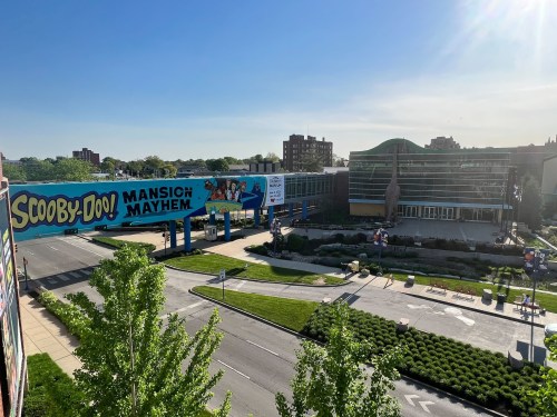 A view of a building with a large "Scooby-Doo! Mansion of Mayhem" banner and green landscaping under a clear blue sky.