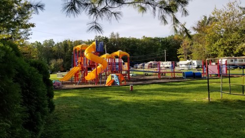 Colorful playground with slides and climbing structures, surrounded by green grass and trees.