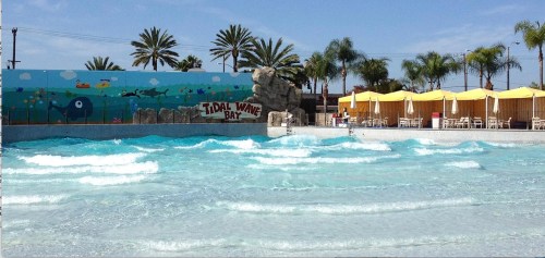 A wave pool with gentle waves, palm trees, and yellow umbrellas in the background, featuring a mural of sea life.