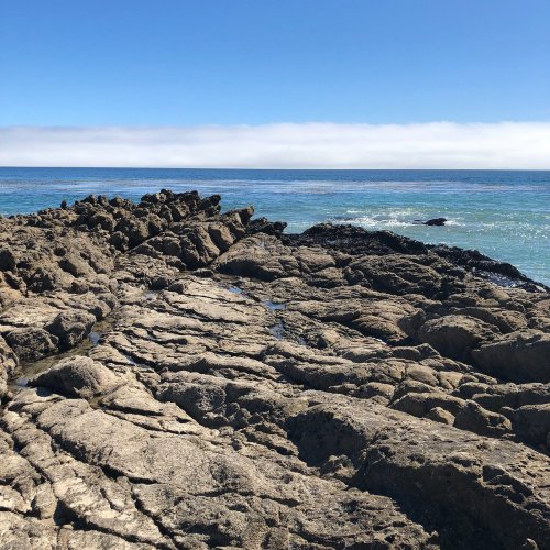 Rocky shoreline extending into calm blue waters under a clear sky.