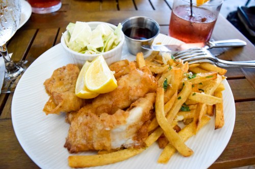 A plate of crispy fried fish with lemon, served with fries and a side of coleslaw and dipping sauce.