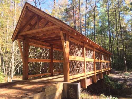 A wooden covered bridge with a rustic design, surrounded by trees in a serene forest setting.