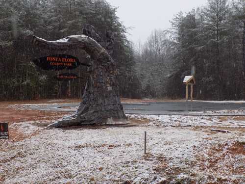 A large, artistic sign resembling a wave marks the entrance to Fonta Flora County Park, surrounded by snow-covered trees.