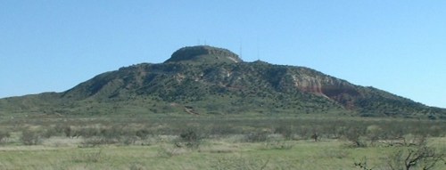 A flat-topped mountain rises above a grassy plain under a clear blue sky.