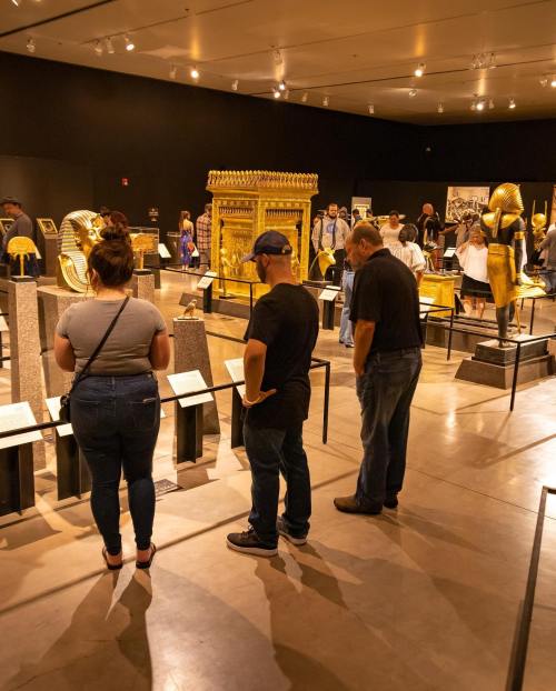 Visitors admire ancient artifacts in a museum exhibit featuring gold items and historical displays.