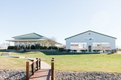 A scenic view of two buildings with a green lawn and a wooden bridge in the foreground under a clear blue sky.