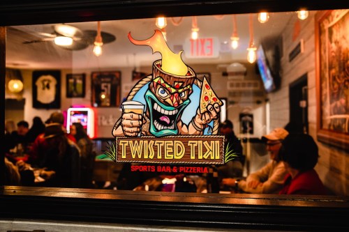 A vibrant sign for Twisted Tiki Sports Bar & Pizzeria, featuring a tiki character holding a drink and pizza slice.