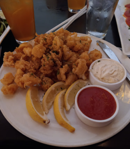 A plate of fried calamari with lemon wedges and two dipping sauces, one creamy and one marinara.