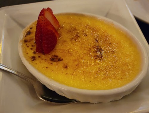 A creamy crème brûlée topped with caramelized sugar and a slice of strawberry, served in a white dish.