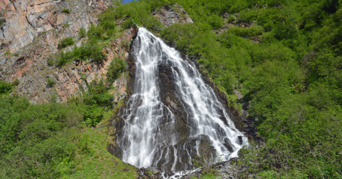A cascading waterfall flows down a rocky cliff, surrounded by lush green vegetation.