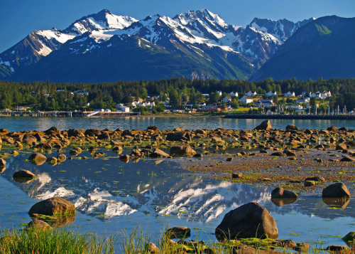 A serene landscape featuring mountains, a calm lake reflecting the peaks, and a small town nestled among trees.