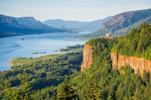 A scenic view of a river winding through lush green hills and cliffs under a clear blue sky.
