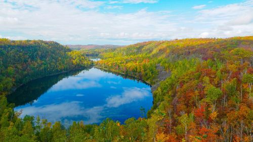 A serene lake surrounded by vibrant autumn foliage and rolling hills under a partly cloudy sky.