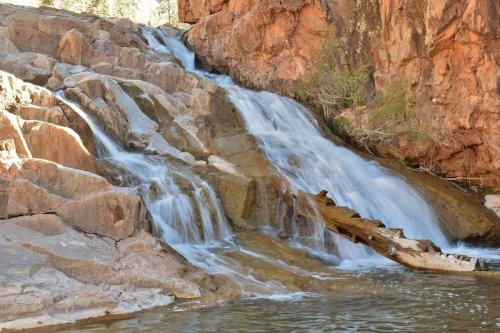 A serene waterfall cascading over rocky terrain into a calm pool, surrounded by rugged cliffs and greenery.