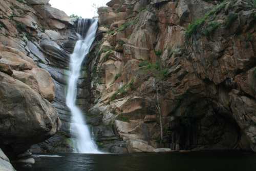 A serene waterfall cascading down rocky cliffs into a calm pool below, surrounded by lush greenery.