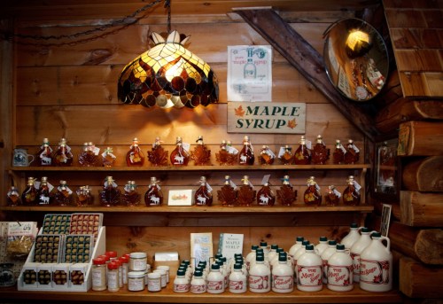 A wooden display featuring various bottles of maple syrup and related products, illuminated by a decorative lamp.
