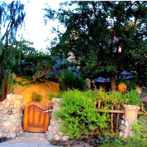 A rustic wooden gate surrounded by lush greenery and stone walls, leading to a charming garden.