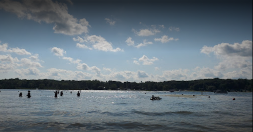 A serene lake scene with people swimming and enjoying the water under a partly cloudy sky.