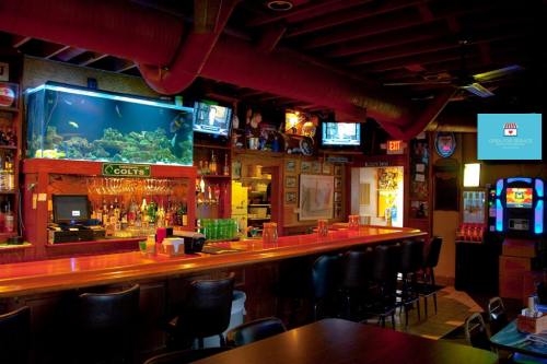 A cozy bar interior featuring an aquarium, a long counter, and multiple TVs displaying various channels.