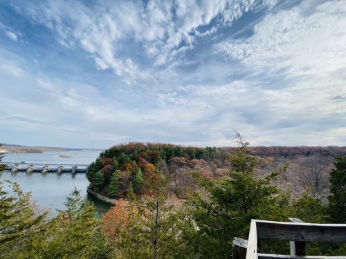 Scenic view of a river winding through trees, with a cloudy sky and a distant dam visible.