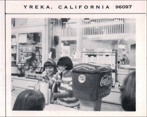 Two girls with bobbed hair smile while serving drinks at a vintage soda fountain in Yreka, California.