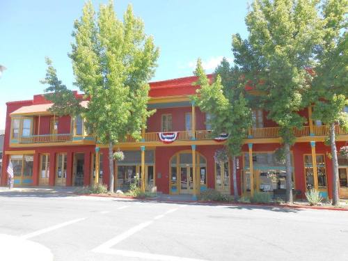 Colorful historic building with trees, red and yellow accents, and decorative bunting in a sunny town setting.