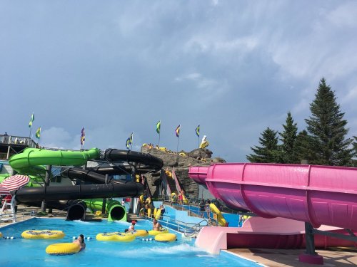 A water park scene featuring colorful slides, a pool with floaties, and cloudy skies in the background.