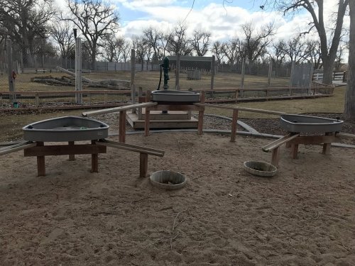 Three sandboxes on wooden platforms in a park, surrounded by bare trees and a cloudy sky.