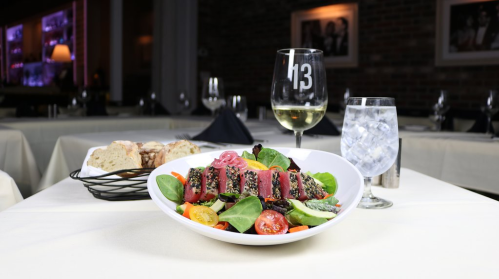 A fresh salad with seared tuna, cherry tomatoes, and greens, accompanied by a glass of white wine and a basket of bread.