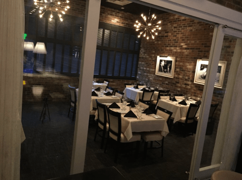 Elegant restaurant interior with tables set for dining, featuring brick walls and modern light fixtures.