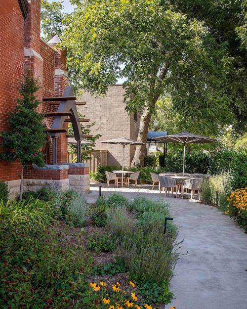 A serene outdoor space with tables under umbrellas, surrounded by greenery and colorful flowers.