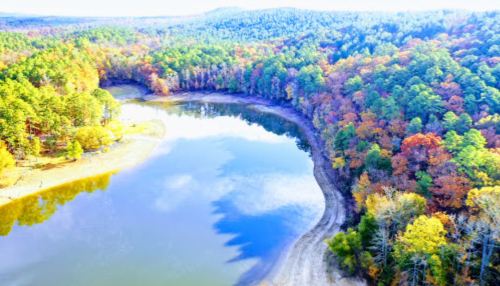 Aerial view of a serene lake surrounded by vibrant autumn foliage and lush green trees.