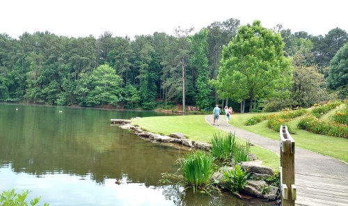 A serene lake surrounded by greenery, with a walking path and people strolling along the water's edge.