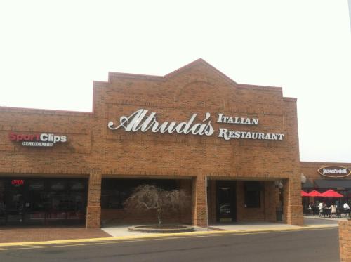 Sign for Atruda's Italian Restaurant on a brick building, with Sport Clips nearby and outdoor seating visible.
