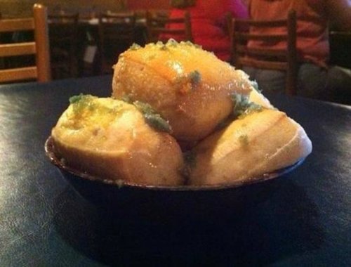 A bowl of fluffy rolls topped with a shiny glaze and green herbs, sitting on a blue table.