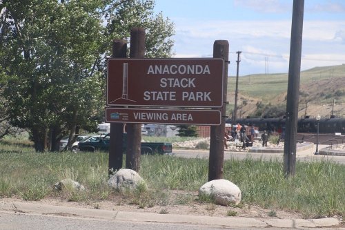 Sign for Anaconda Stack State Park Viewing Area, surrounded by grass and trees, with a cloudy sky in the background.