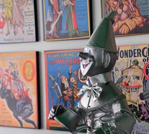 A metallic toy figure of a character stands in front of colorful vintage posters featuring "The Wizard of Oz."