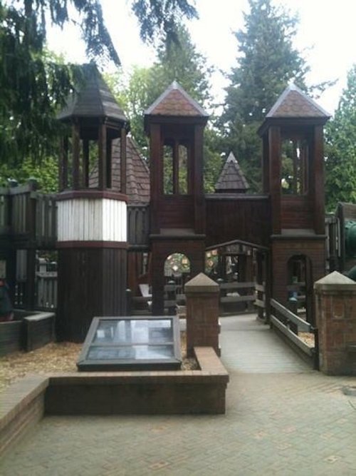 A wooden playground structure with towers, bridges, and surrounding trees, inviting for children's play.